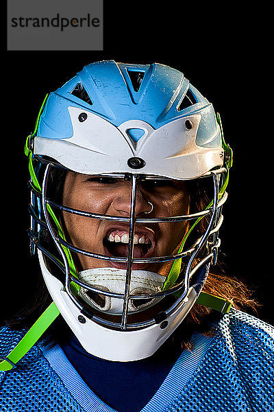 Junger männlicher Lacrosse-Spieler mit Lacrosse-Helm schreit  Nahaufnahme-Portrait vor schwarzem Hintergrund