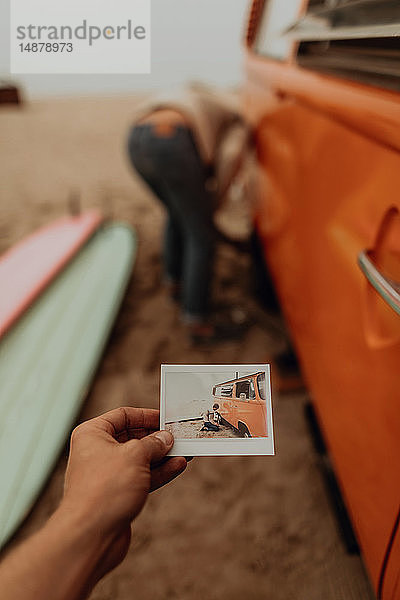 Junge Frau hält ein Sofortfoto von ihrem Freund  der einen platten Reifen an einem Wohnmobil am Strand entfernt  Jalama  Kalifornien  USA
