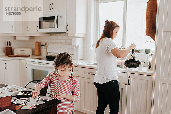 Mädchen arrangiert Karten in der Küche  Mutter gießt heißes Wasser im Hintergrund