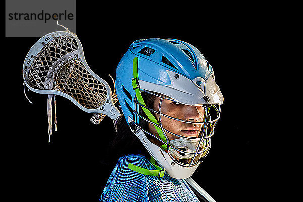 Junger männlicher Lacrosse-Spieler mit Lacrosse-Schläger  Portrait vor schwarzem Hintergrund