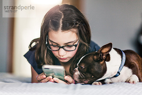 Mädchen benutzt Smartphone neben Haushund im Bett