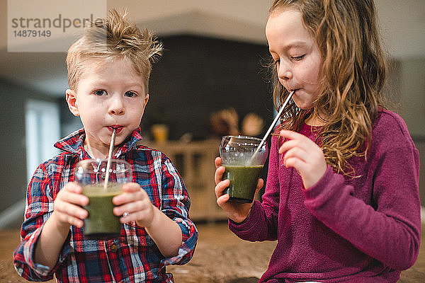 Kinder trinken grünen Saft mit Strohhalm