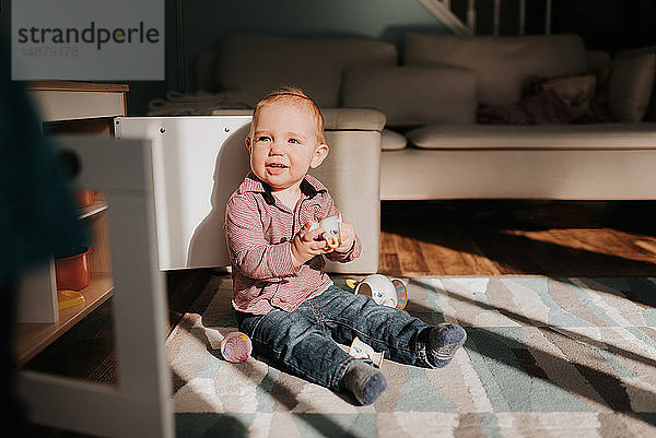 Kleiner Junge sitzt spielend auf Wohnzimmerteppich