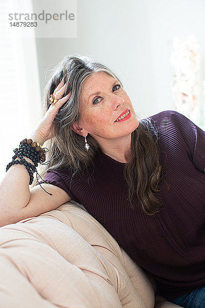 Stilvolle reife Frau mit langen grauen Haaren auf Sofa sitzend  Porträt