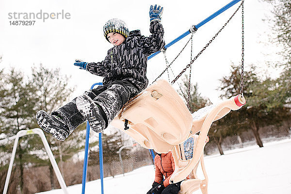 Junge springt von Spielplatzschaukel im Schnee