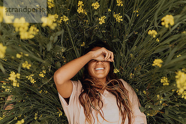 Junge Frau im gelben Wildblumenfeld liegend  Überkopfporträt  Jalama  Kalifornien  USA