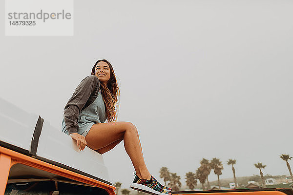 Junge Frau sitzt auf dem Dach eines Wohnmobils am Strand  Jalama  Kalifornien  USA