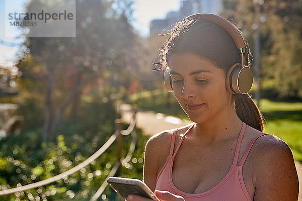 Frau  die im Stadtpark mit Kopfhörern Musik hört