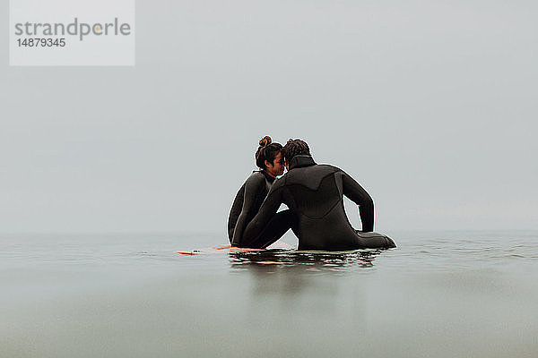 Junges Surferpaar sitzt auf Surfbrettern in ruhiger  nebliger See  Ventura  Kalifornien  USA