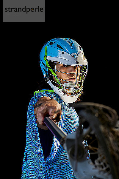 Junger männlicher Lacrosse-Spieler beim Longieren mit Lacrosse-Stick  Portrait vor schwarzem Hintergrund