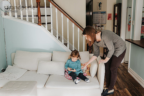 Weibliches Kleinkind betrachtet das Smartphone der Mutter auf dem Wohnzimmersofa