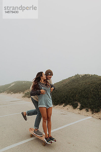 Junges Paar teilt sich ein Skateboard auf einem Strandparkplatz  Jalama  Kalifornien  USA