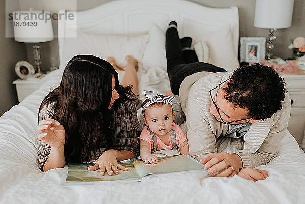 Ehepaar liest mit der kleinen Tochter auf dem Bett im Schlafzimmer