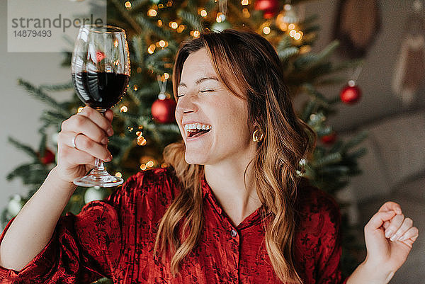 Frau tanzt mit Wein neben geschmücktem Weihnachtsbaum