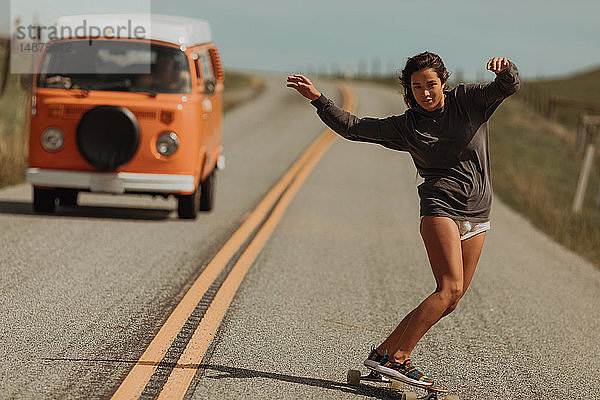 Junge Skateboardfahrerin schwenkt mit dem Skateboard die Landstrasse hinunter  gefolgt von einem Wohnmobil  Jalama  Kalifornien  USA