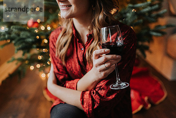 Frau trinkt Wein neben geschmücktem Weihnachtsbaum