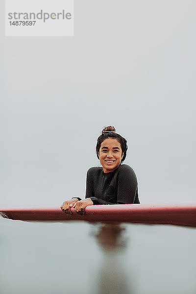 Junge Surferin lehnt auf einem Surfbrett in ruhiger  nebliger See  Porträt  Ventura  Kalifornien  USA