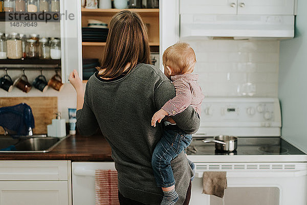 Mutter trägt einen kleinen Sohn  der in der Küche Essen zubereitet  Rückansicht