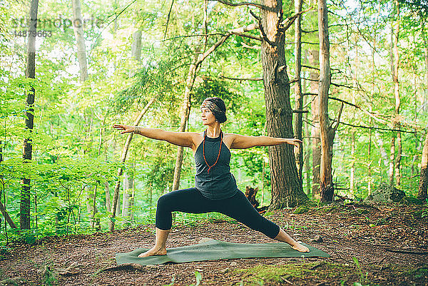 Frau macht Kriegerpose im Wald