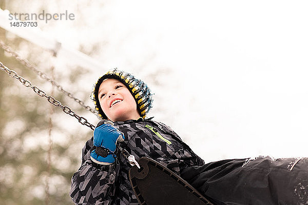 Junge mit Strickmütze schwingt im Winter auf der Spielplatzschaukel