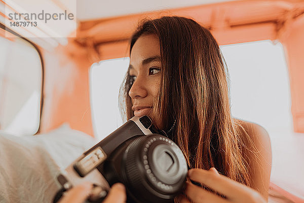 Junge Frau  die eine Sofortbildkamera auf dem Rücksitz eines Wohnmobils hochhält  Jalama  Kalifornien  USA