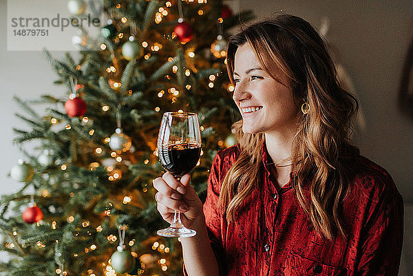 Frau trinkt Wein neben geschmücktem Weihnachtsbaum