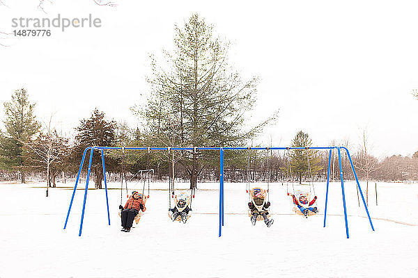 Mann und Kinder schaukeln auf einer Reihe von Spielplatzschaukeln im Schnee