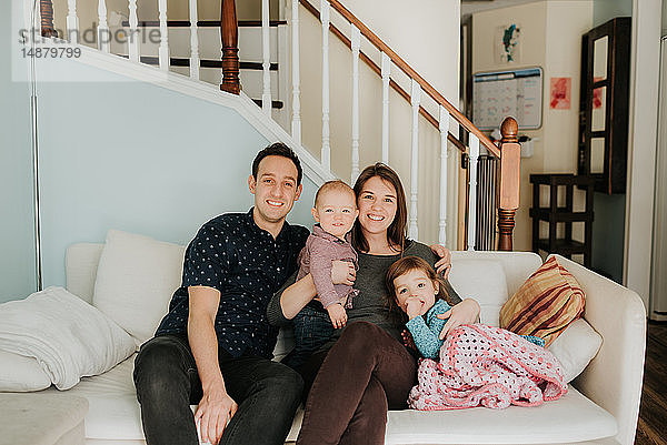 Mittelgroßes erwachsenes Paar auf dem Sofa mit Baby-Sohn und Kleinkind-Tochter  Porträt