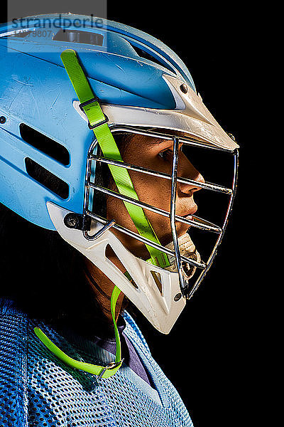 Junger männlicher Lacrosse-Spieler mit Lacrosse-Helm  Nahaufnahme-Portrait vor schwarzem Hintergrund