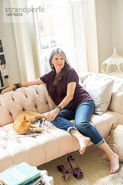 Stilvolle reife Frau auf Sofa sitzend mit Ingwer-Katze