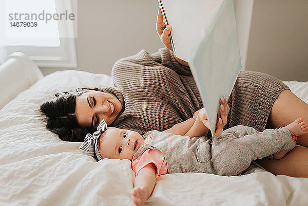Mutter liest mit der kleinen Tochter auf dem Bett im Schlafzimmer