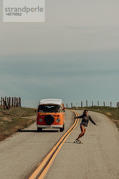 Junge Skateboarderin fährt auf einer Landstrasse Skateboard  gefolgt von einem Freizeitfahrzeug  Jalama  Kalifornien  USA