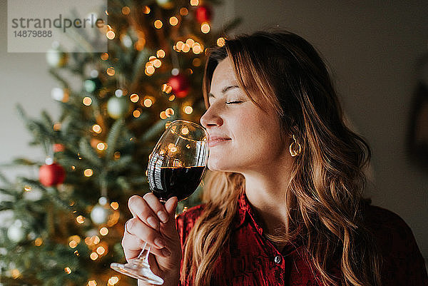 Frau riecht an einem Glas Wein neben einem geschmückten Weihnachtsbaum