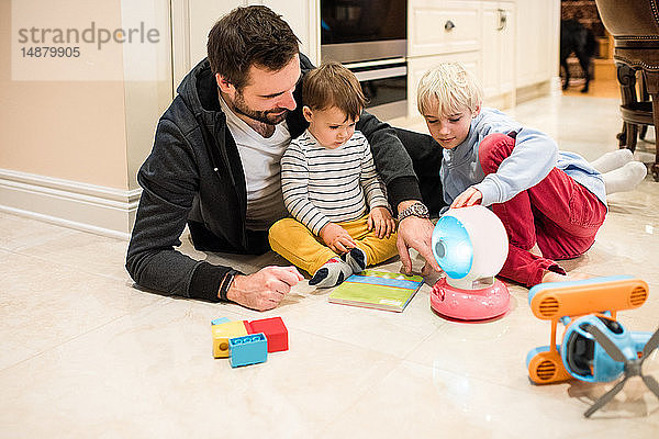 Vater und Söhne spielen mit Spielzeug auf dem Boden
