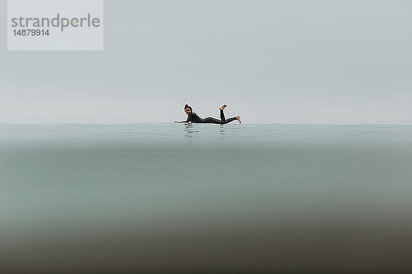 Junge Surferin auf einem Surfbrett liegend in ruhiger  nebliger See  Portrait in voller Länge  Ventura  Kalifornien  USA