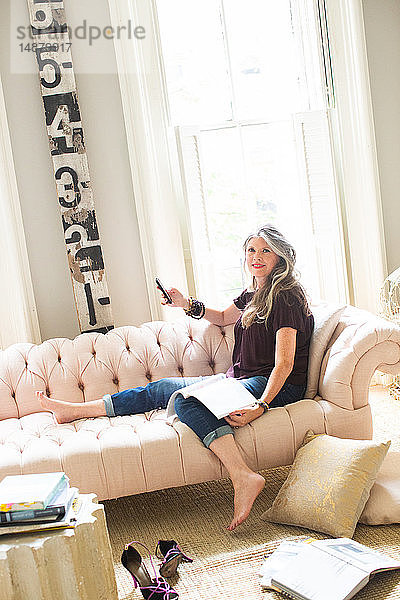 Stilvolle reife Frau sitzt auf Sofa und hält Smartphone  Porträt