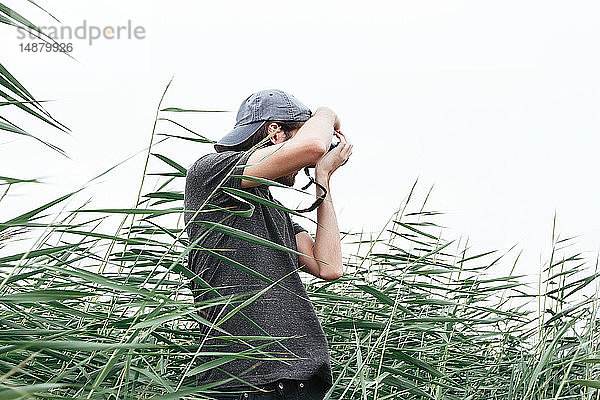 Mann mit Kamera beim Fotografieren im hohen Gras