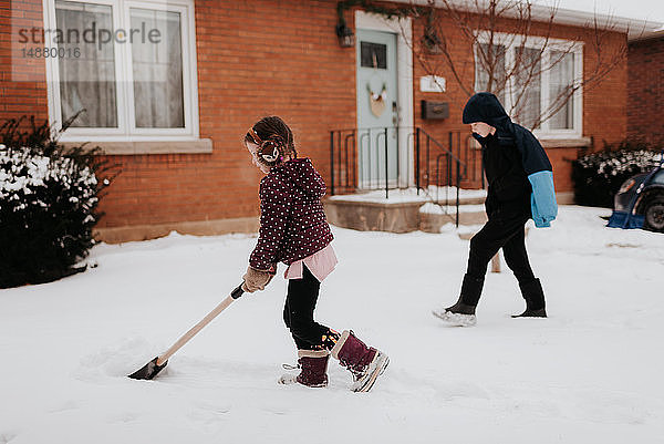 Kinder schaufeln Schnee vor dem Haus