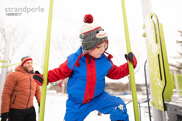 Junge mit Vater klettert auf Spielplatzrutsche im Schnee