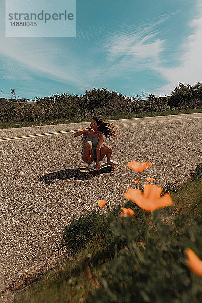 Junge Skateboardfahrerin hockt auf einer Landstraße  Jalama  Kalifornien  USA