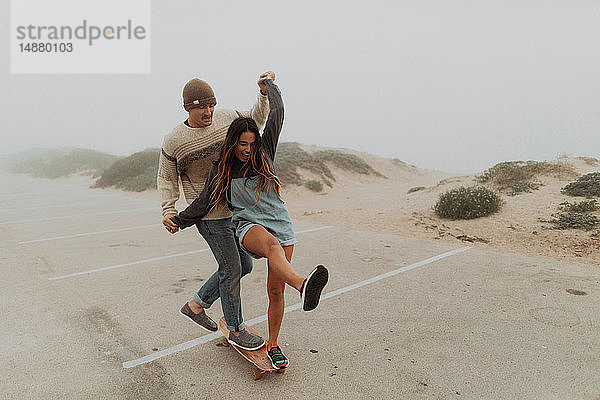 Junges Paar hält Händchen und teilt sich ein Skateboard auf einem Strandparkplatz  Jalama  Kalifornien  USA