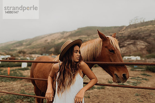 Junge Frau mit Filzhut lehnt neben Pferd am Zaun  Jalama  Kalifornien  USA