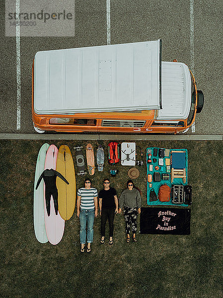 Drei junge Surfer mit Surfausrüstung und Freizeitfahrzeug auf dem Rücken liegend am Strandparkplatz  Portrait von oben  Ventura  Kalifornien  USA
