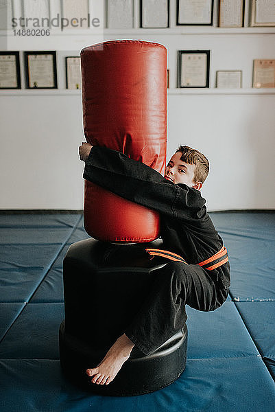 Junge klammert sich im Kampfsportstudio an den Sandsack
