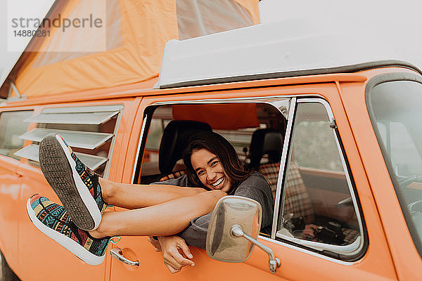 Junge Frau mit Beinen durch das Fenster eines Wohnmobils am Strand  Portrait  Jalama  Kalifornien  USA