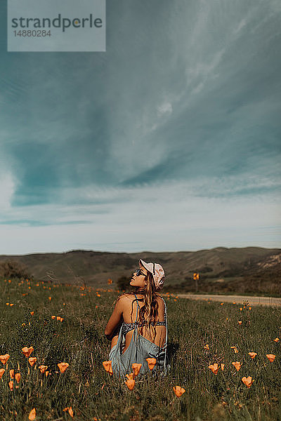 Junge Frau sitzt auf einem Feld mit Wildblumen und schaut nach oben  Jalama  Kalifornien  USA