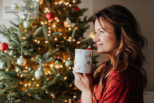 Frau trinkt Kaffee neben geschmücktem Weihnachtsbaum