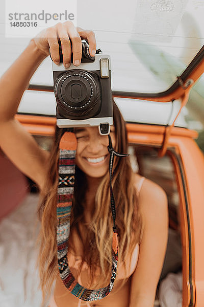 Junge Frau hält Sofortbildkamera auf dem Rücksitz eines Wohnmobils am Strand hoch  Jalama  Kalifornien  USA