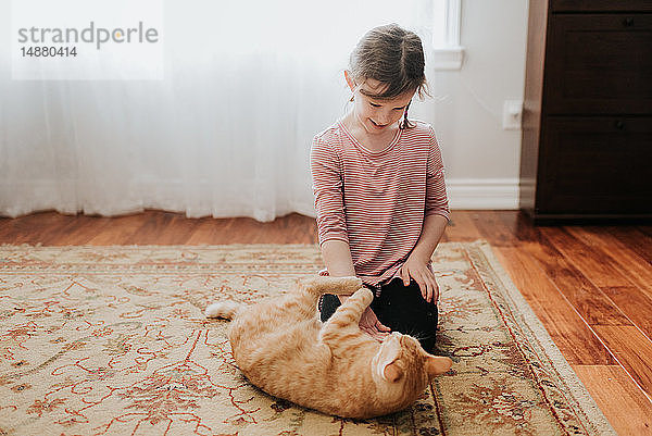 Mädchen spielt zu Hause mit Katze auf Teppich