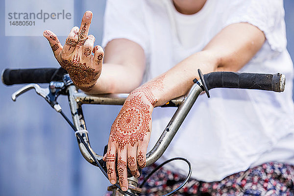 Frau mit Henna-Tattoo an den Händen sitzt auf Fahrrad und macht grobe Geste